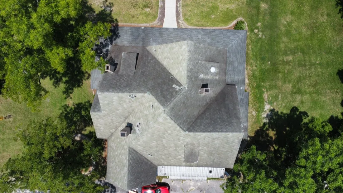 Overhead view of a weathered, green-stained shingle roof with mismatched patched sections, before replacement
