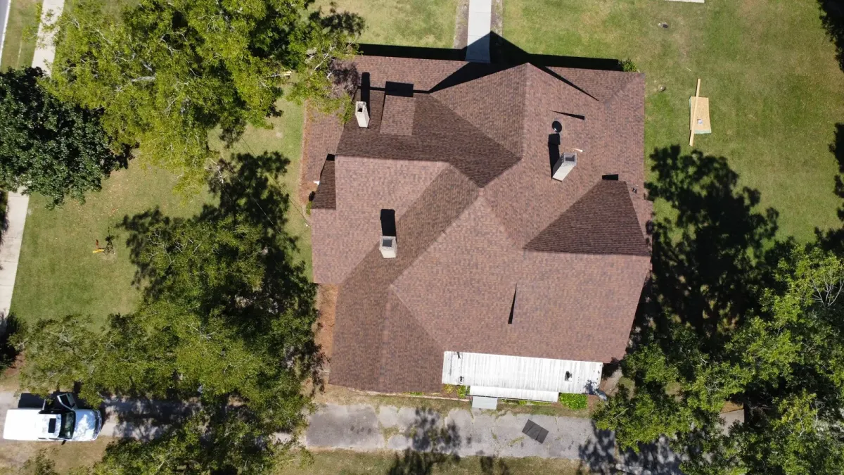 Overhead drone view of a home's freshly laid brown architectural shingle roof, ringed by mature trees
