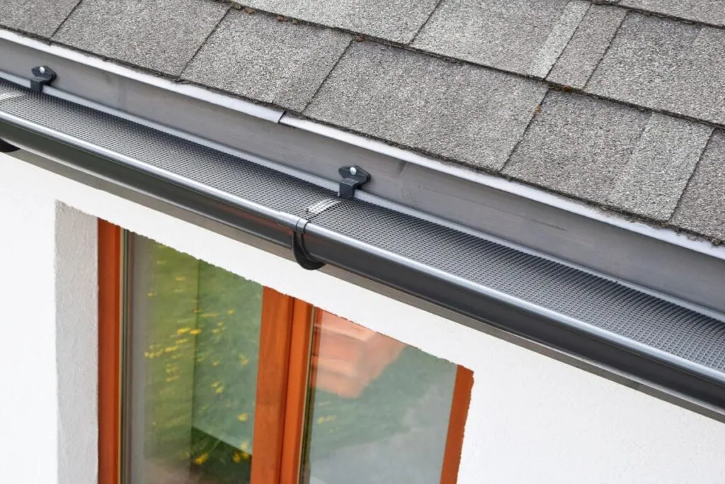 Gutter guard system fitted along a shingle roof edge