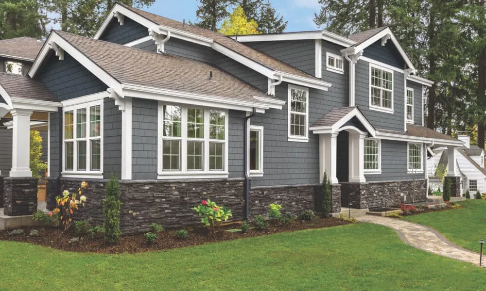 Two-story craftsman home with blue-gray shake siding, white trim, a stone veneer base and shingled roof