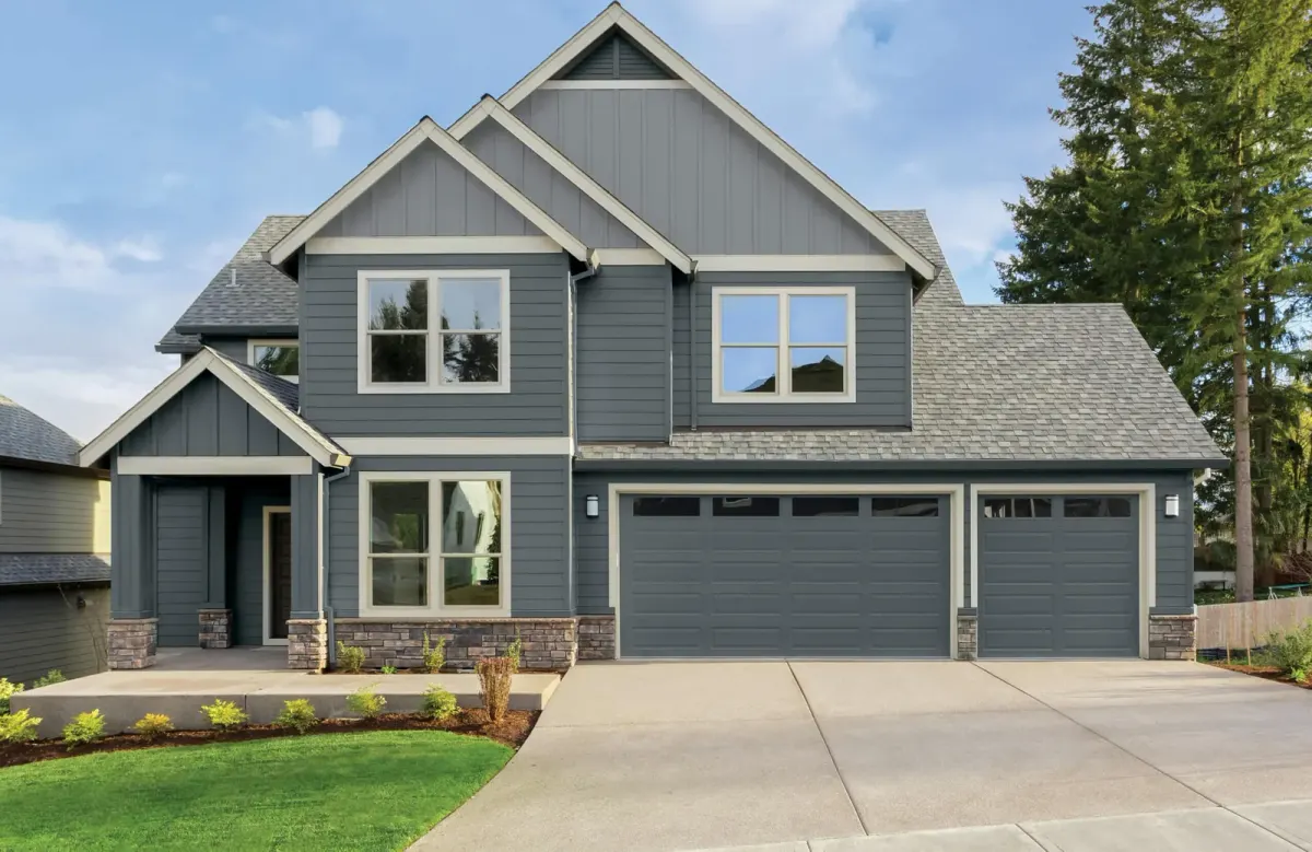 Blue-gray two-story home with board-and-batten gables, stone accents, shingle roof and three garage doors