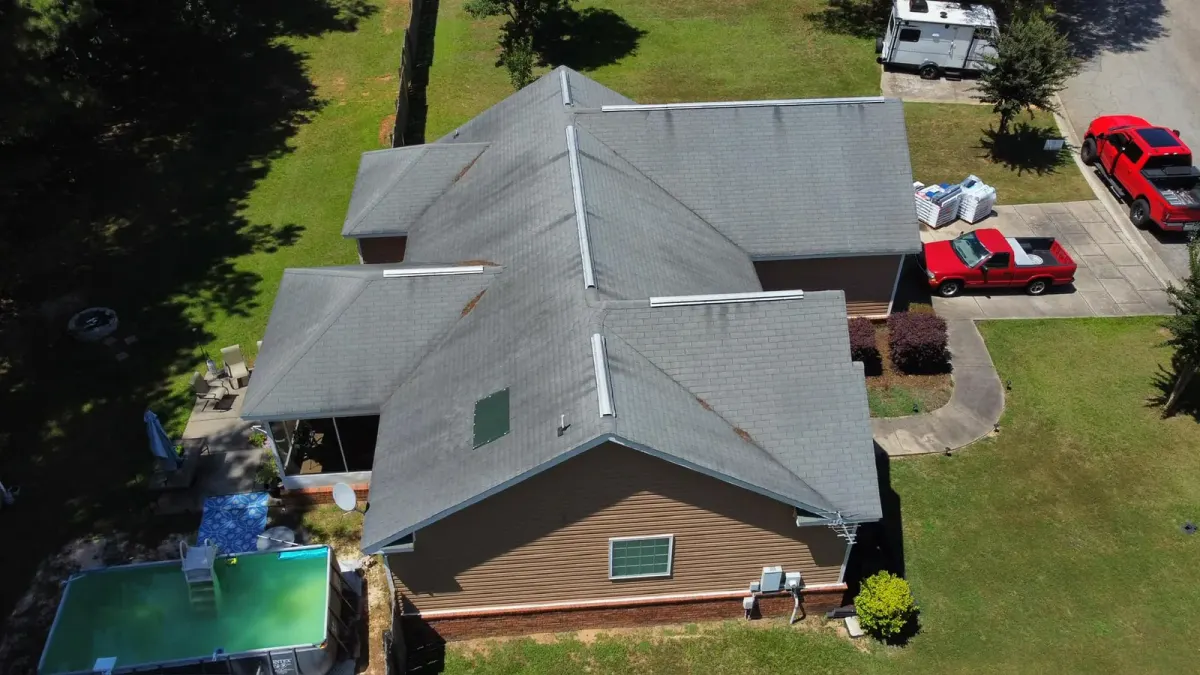 Aerial view of a gray shingled hip roof with shingles torn away in patches along several hip ridges