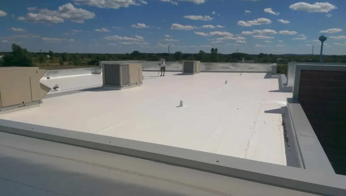 Finished white membrane roof on a commercial building with a lone worker holding a long-handled tool