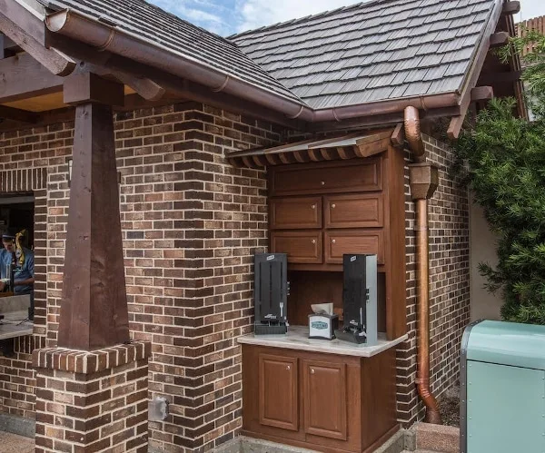 Copper half-round gutter and downspout with a leader box running down the brick wall of an outdoor drink counter