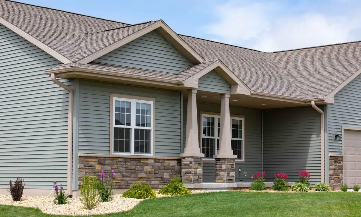 Sage-green lap vinyl siding with tan trim, stone veneer wainscot, and a columned porch on a ranch home